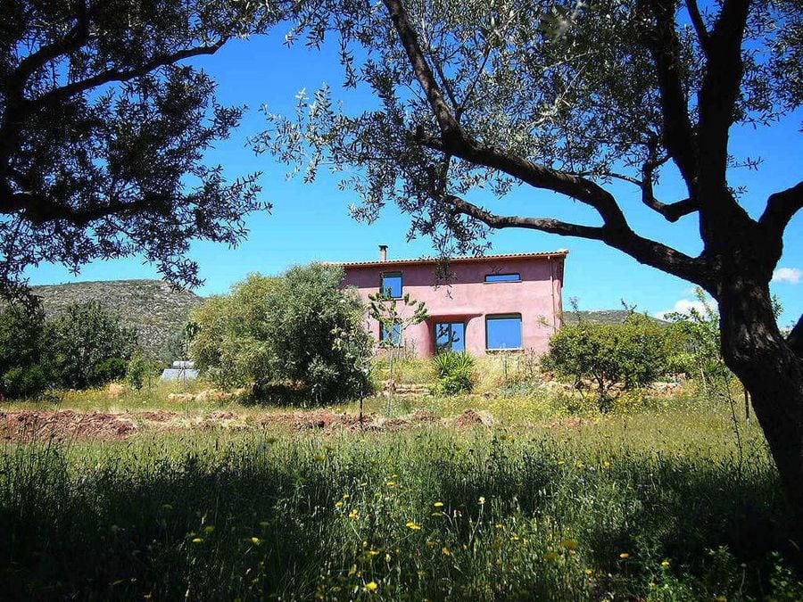 pink building of Korogonas Ark surrounded by green plants and olive trees